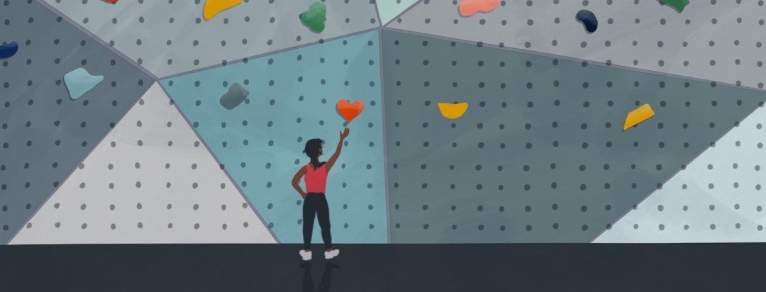 person on ground reaching for a heart shaped rock on a climbing wall