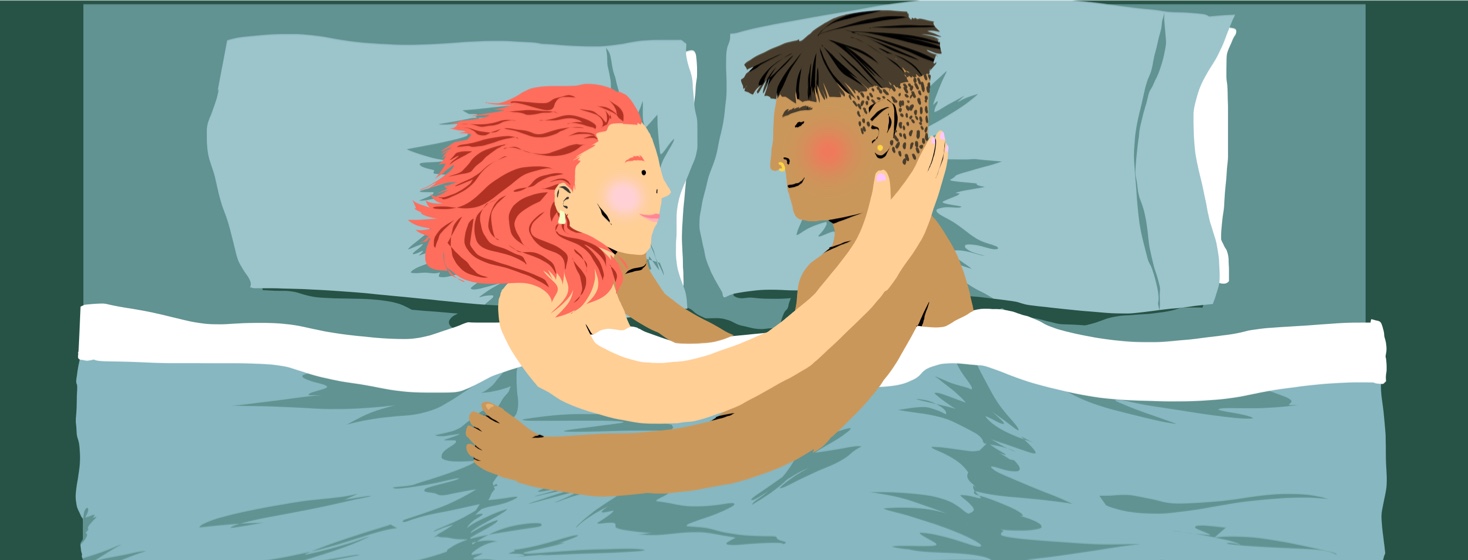 Two people lay under the covers in bed looking at each other